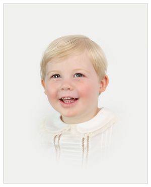 Studio portrait showing a young child with blonde hair smiling warmly while wearing white clothing.