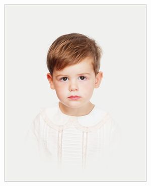 Young child in white outfit with rosy cheeks and soft brown hair against a light background.
