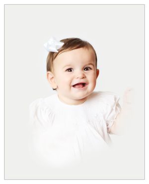 Happy baby in white clothing smiles brightly against clean white background.