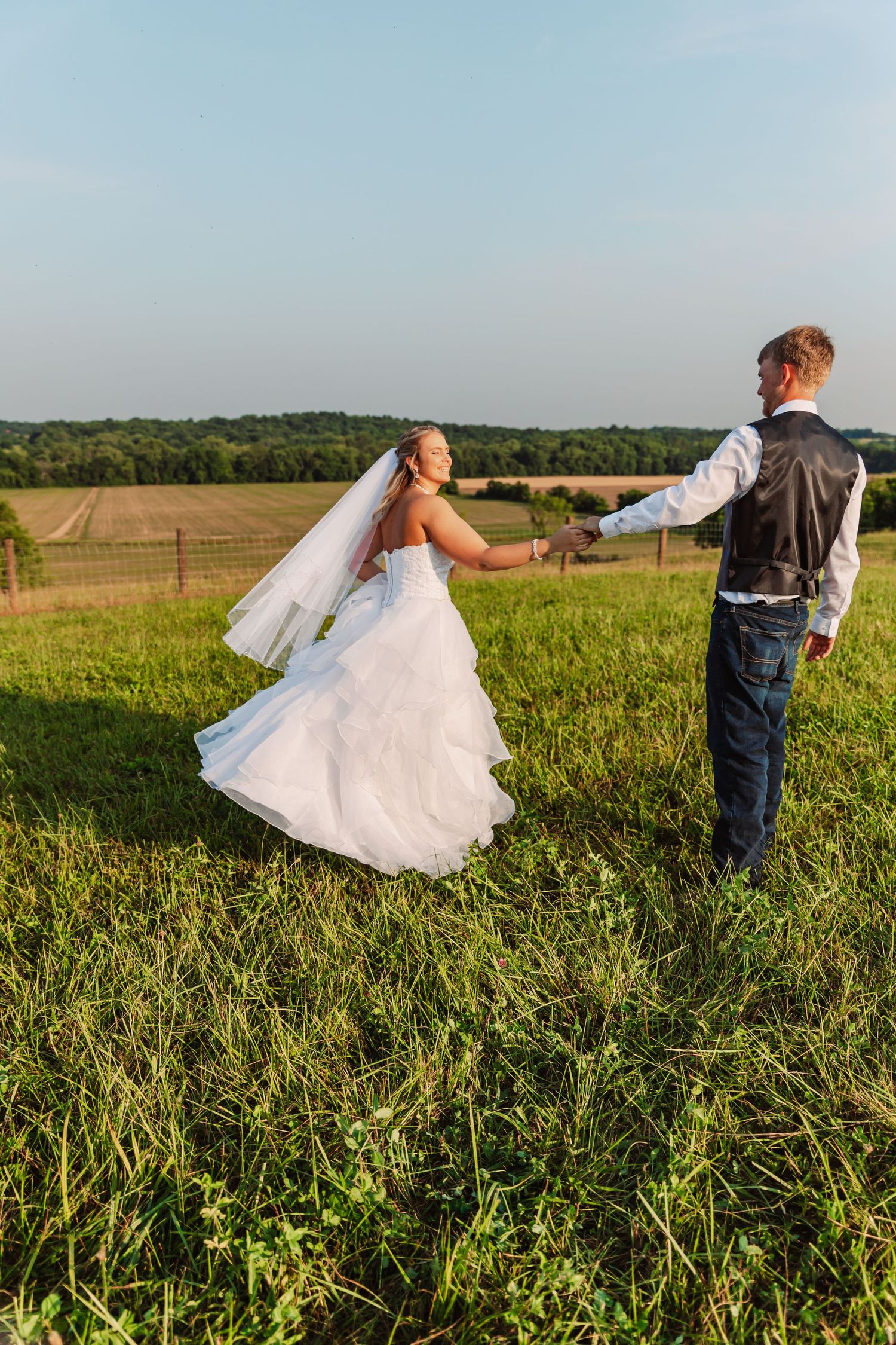 Newlyweds playing and spinning in an open field during golden hour.
