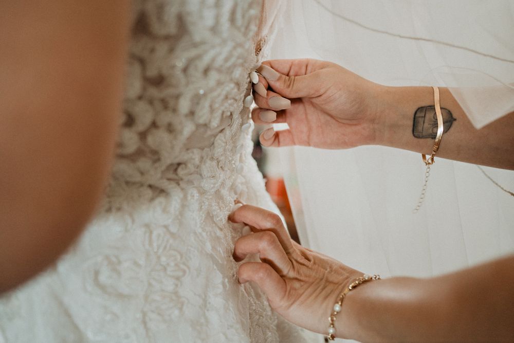 Bride's friend assisting her with the final touches on the wedding dress, showcasing the bond of friendship