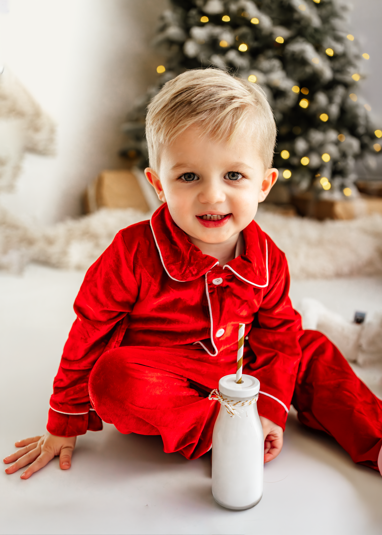 Small child in red velvet dress holds large plush gingerbread man amid Christmas presents and holiday decorations. Christmas Mini Photoshoot