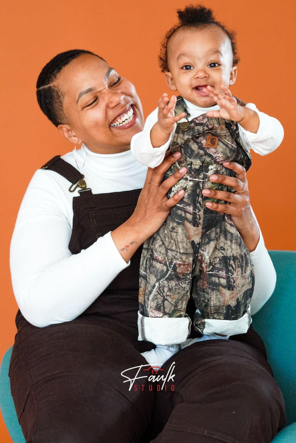 A joyful moment captured against an orange backdrop as parent and child share smiles while wearing coordinating outfits.