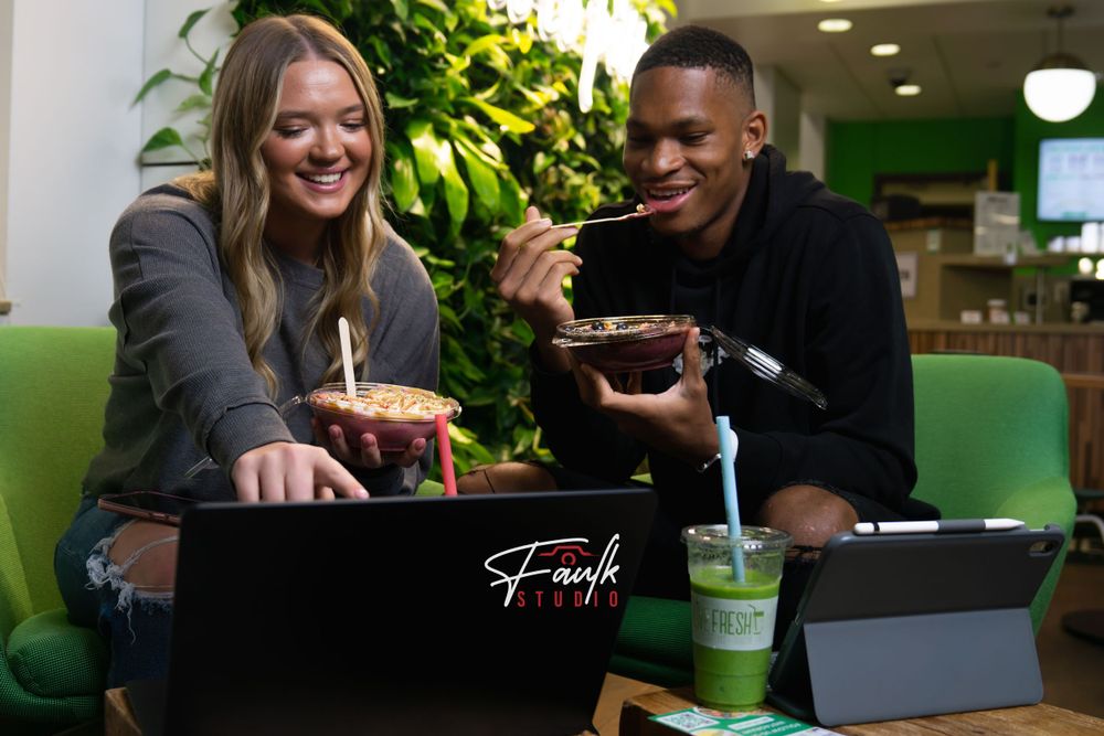 Two people share a meal together while working on laptops at a restaurant table with green drinks.