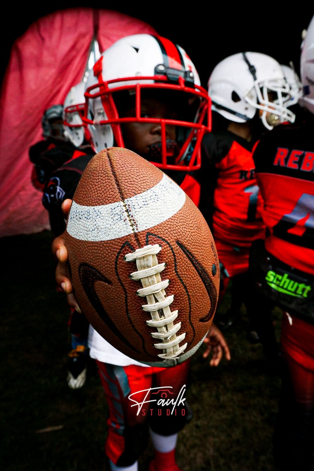 Close-up shots of a brown leather football with white laces against a dark background with red helmets visible.