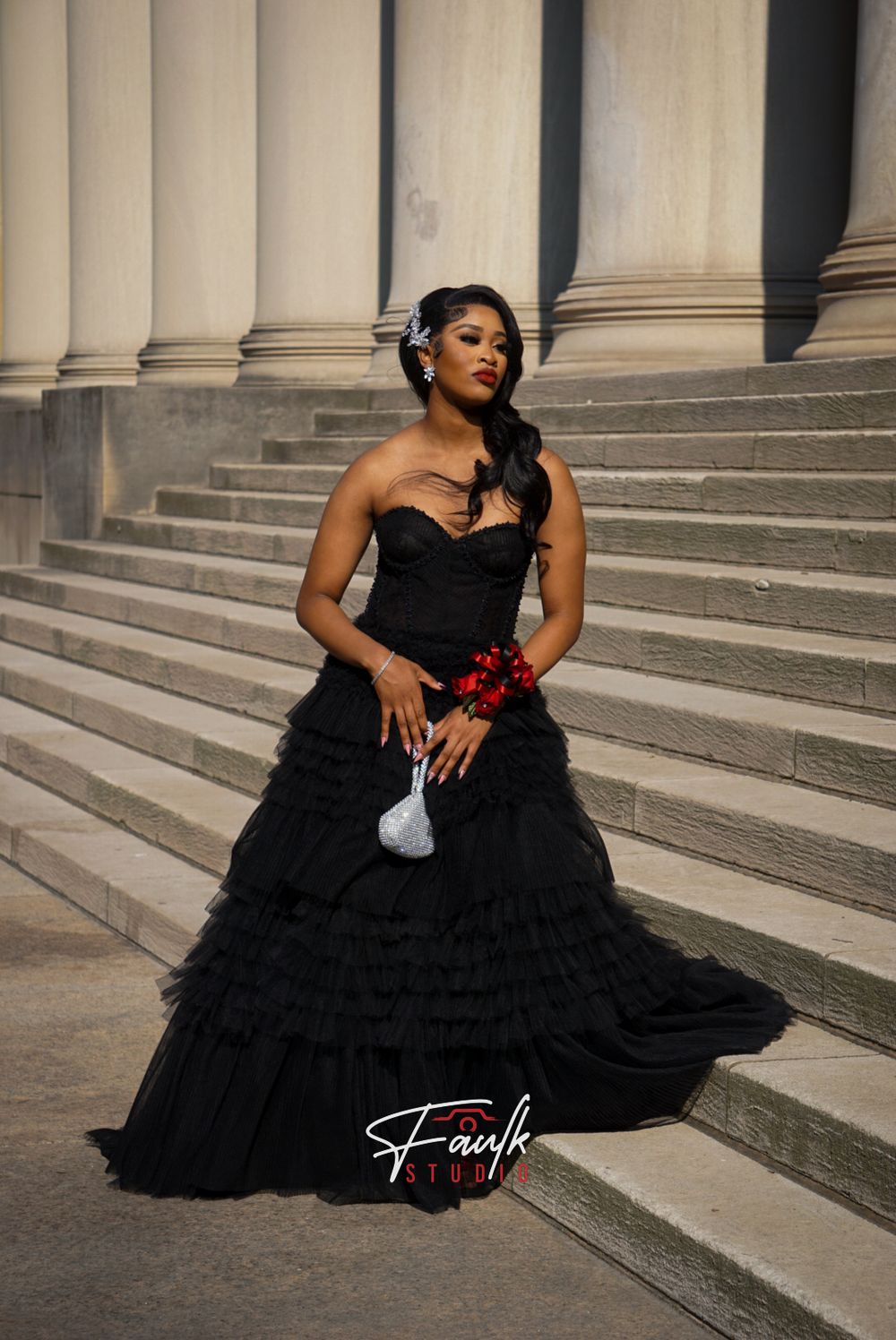 A dramatic black ruffled evening gown with a sweetheart neckline photographed on stone steps with classical columns.