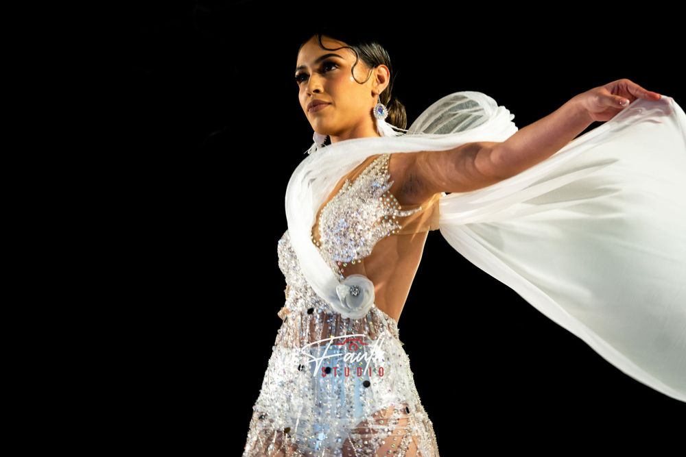 A bride in a white flowing dress with crystal embellishments twirls gracefully against a dark background.