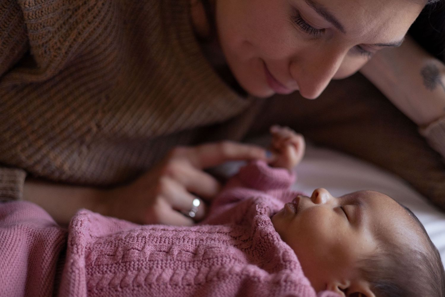 A Mom plays with her sleeping newborns hand.
