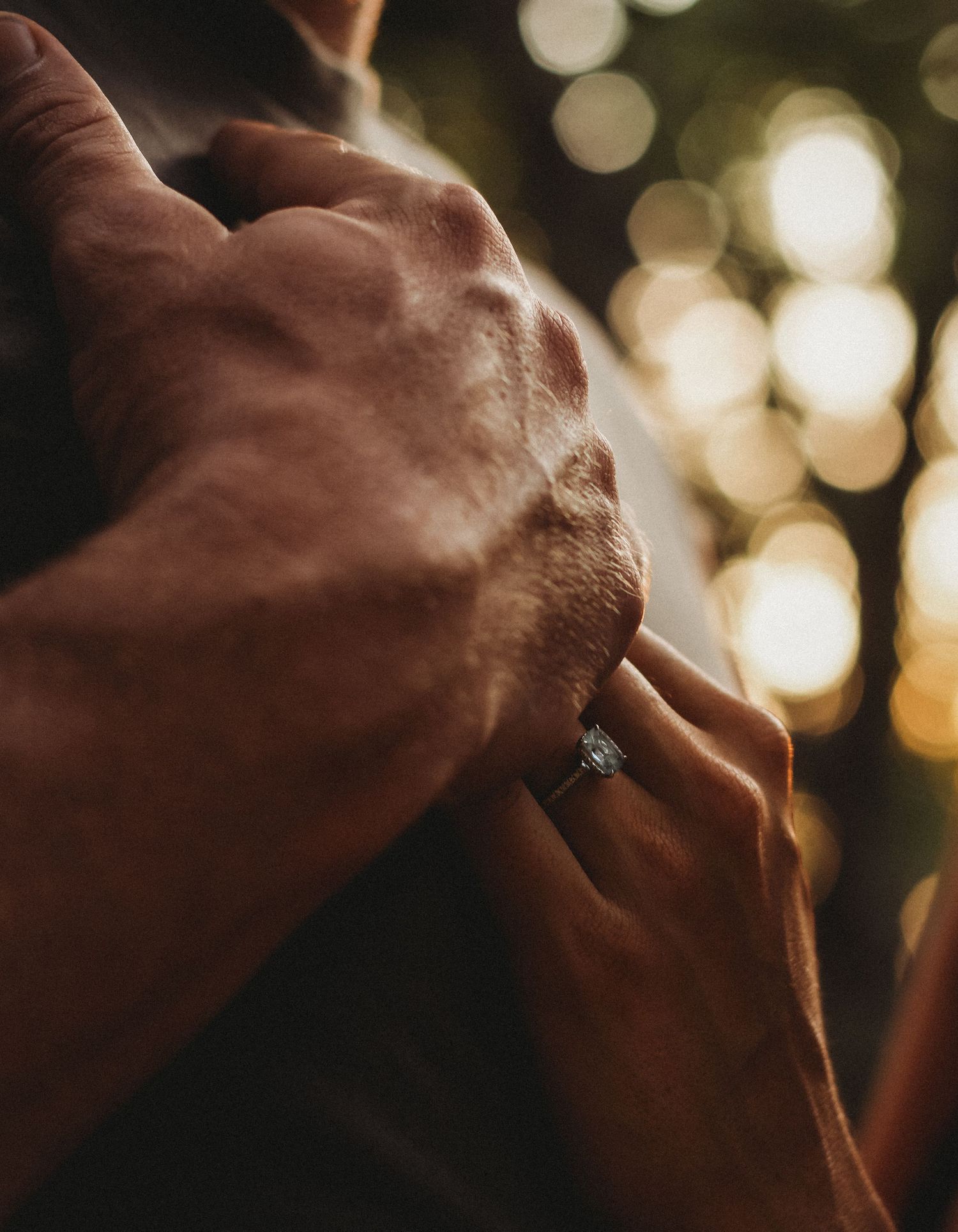 Artistic close-up of hands with engagement ring against blurred bokeh lights.
