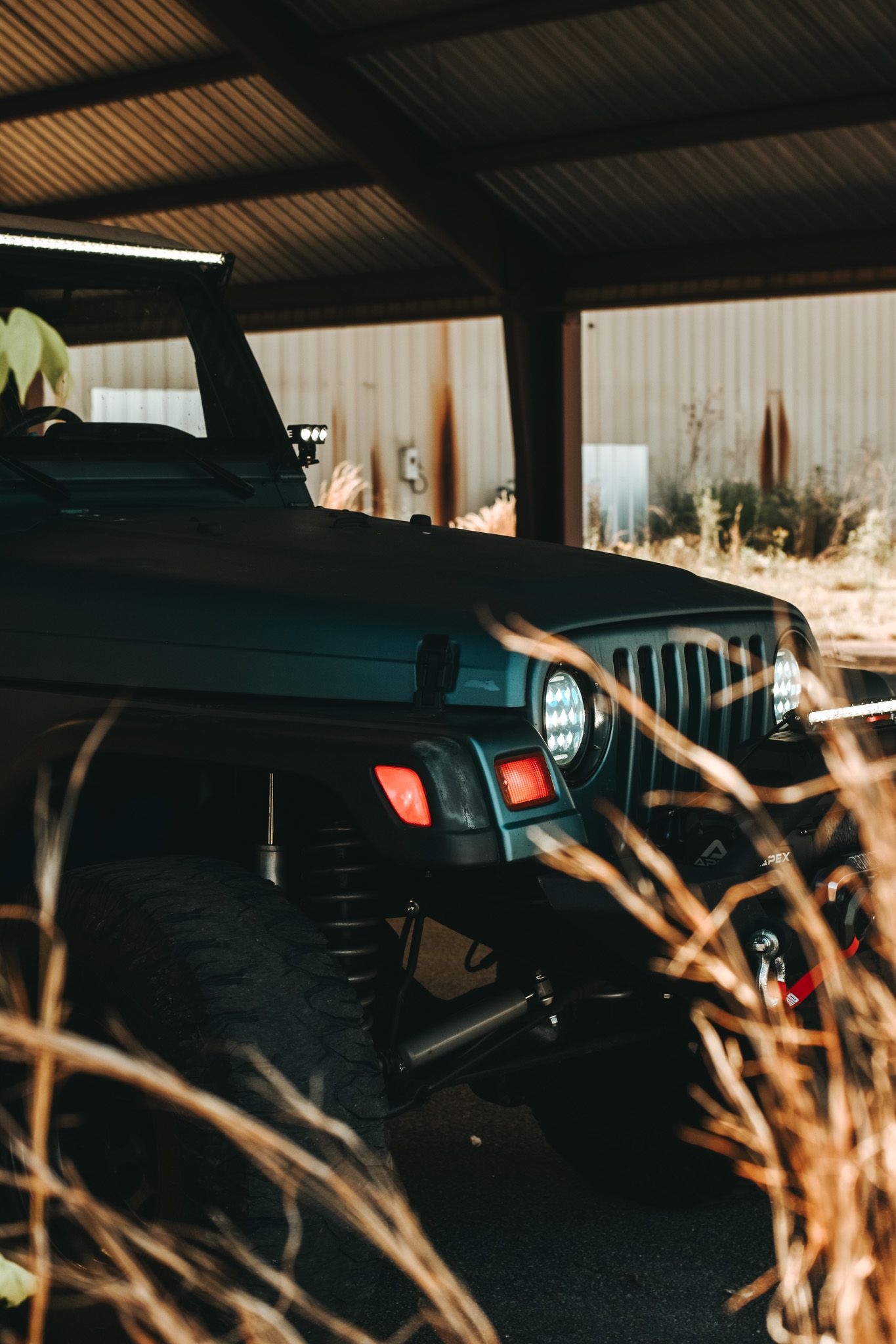 Moody shot of a Jeep's front end with LED lights glowing through dry grass at dusk.
