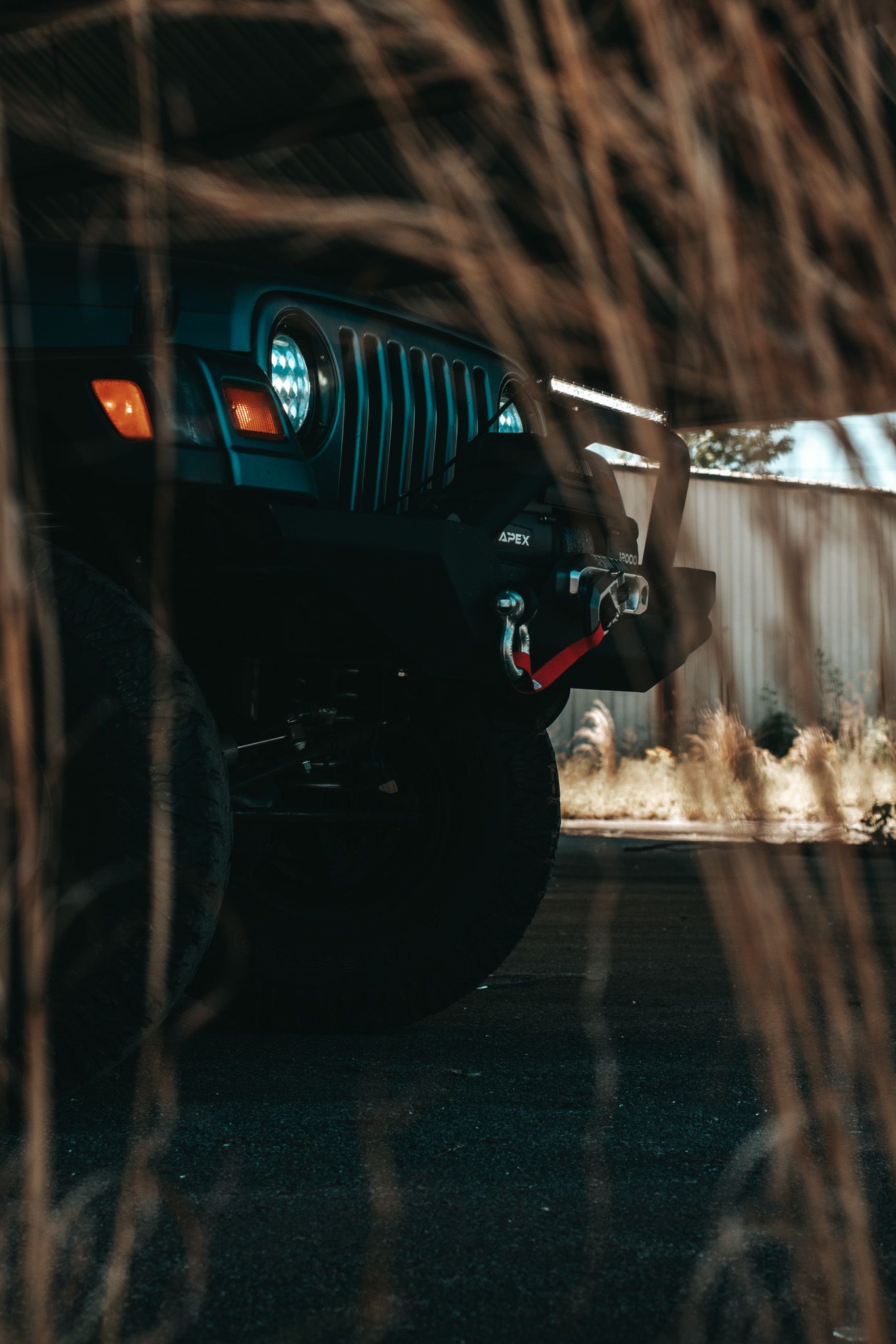 Dramatic view of a Jeep's front grille and headlights through branches at night.