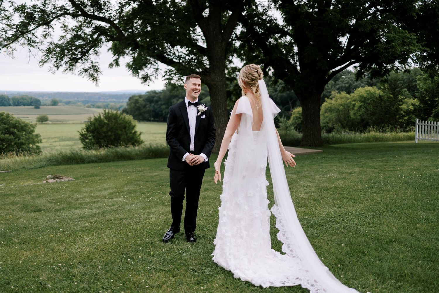 Elegant wedding couple poses on manicured lawn with scenic countryside views.