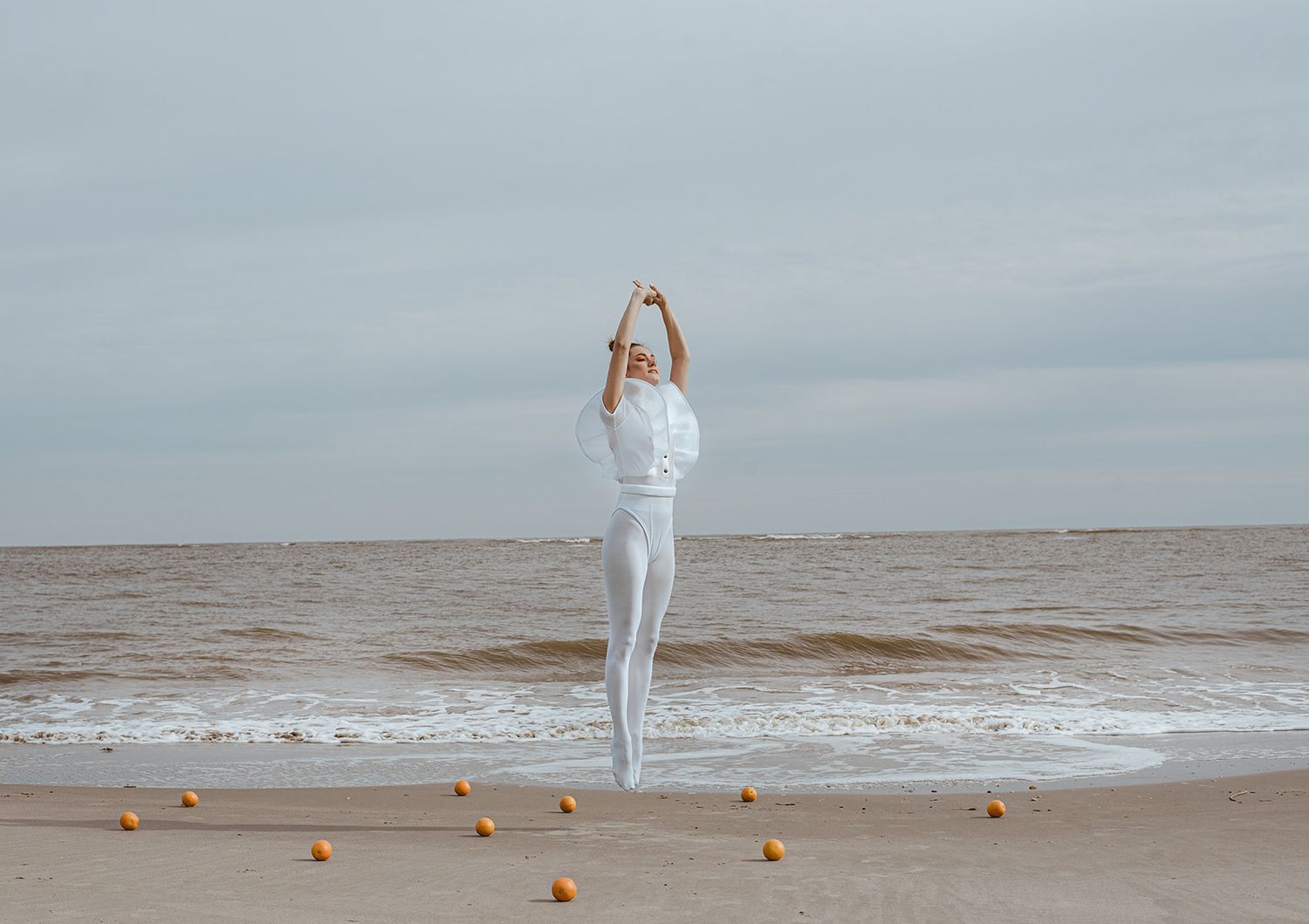A portrait of a girl floating in the air at the beach with oranges all over the ground.