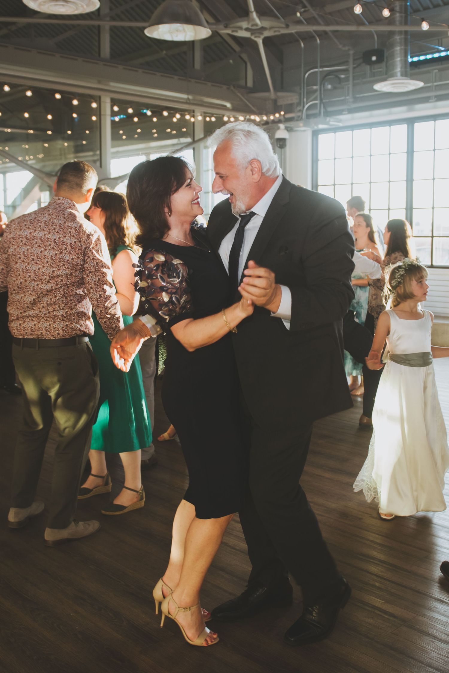 Wedding guests dancing together at an indoor reception with string lights.