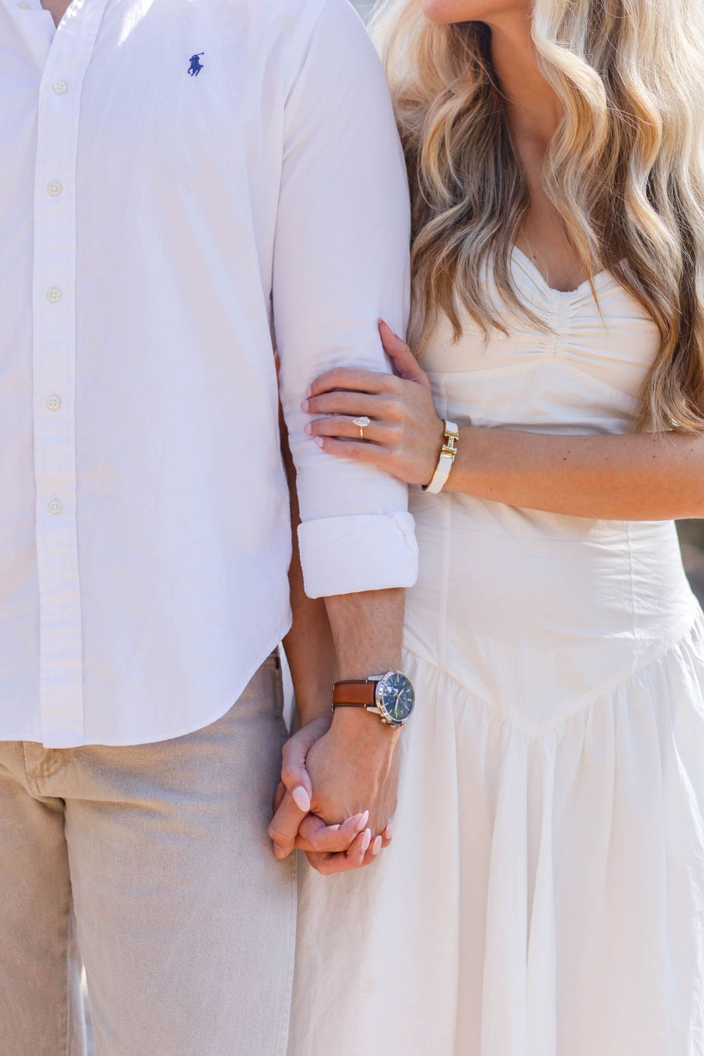 Close-up of couple in white outfits showing engagement ring and watch details.