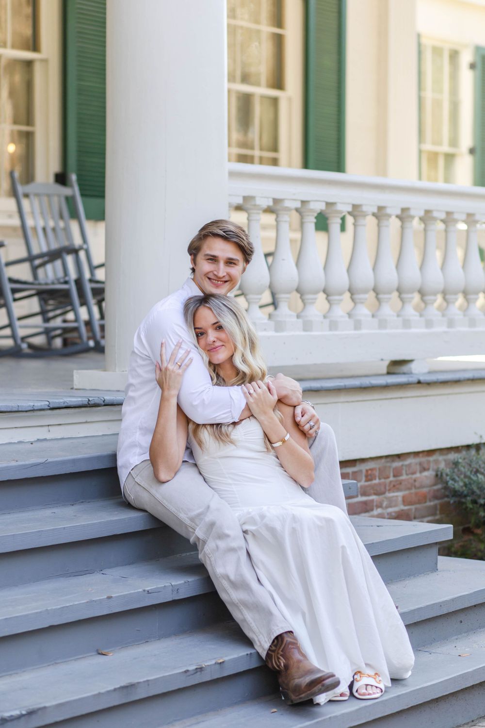 Couple sitting on white porch steps showing off engagement ring.