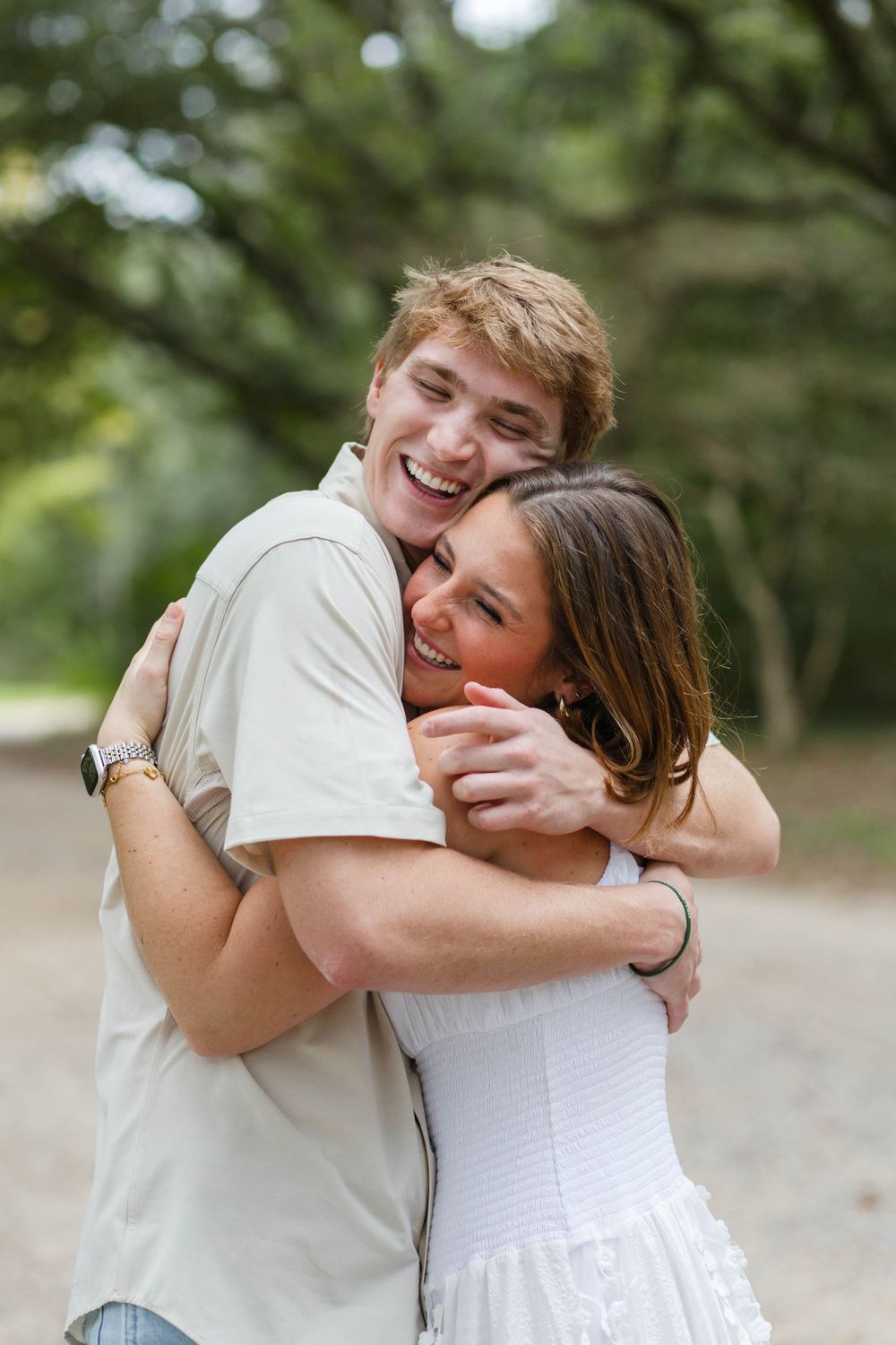 Couple embraces joyfully on dirt path under oak trees.