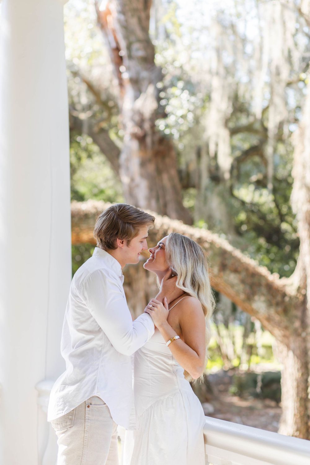 Intimate wedding couple moment under southern plantation columns surrounded by moss-draped trees.