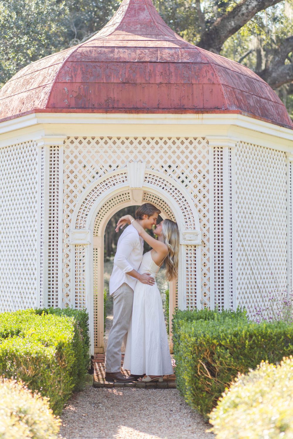 Romantic couple embraces in ornate white gazebo with copper dome roof.