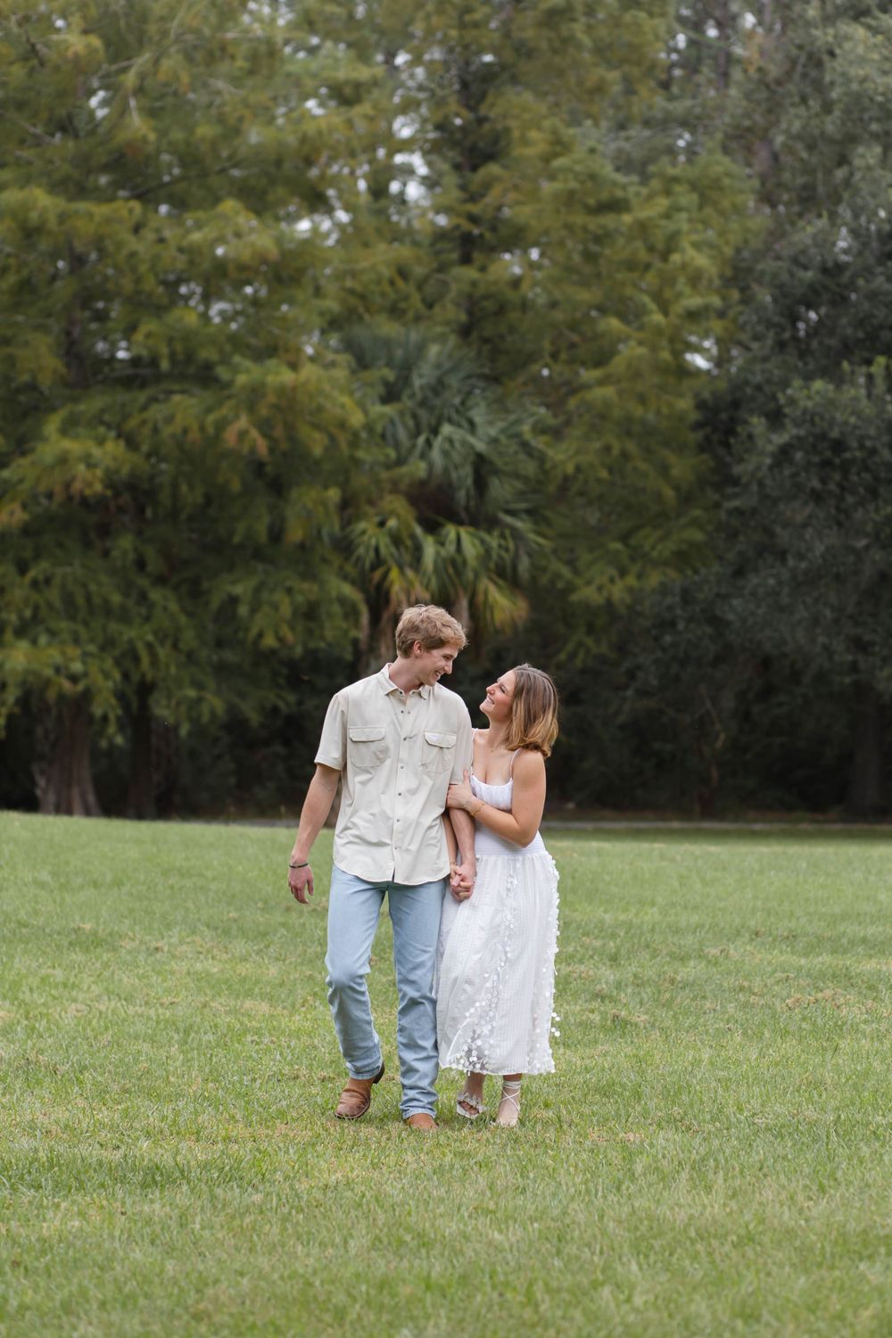 Couple walking together on grassy lawn surrounded by trees.