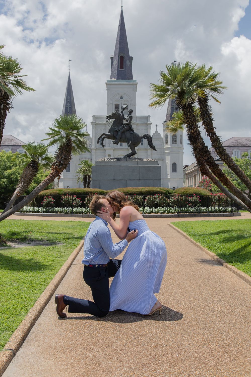 A special moment captures a proposal in front of a historic white church with palm trees and a statue in New Orleans.