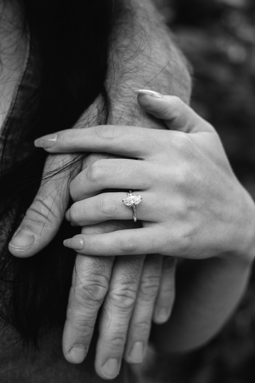 Black and white close-up of two hands, woman wearing a diamond engagement ring, romantic couple moment.