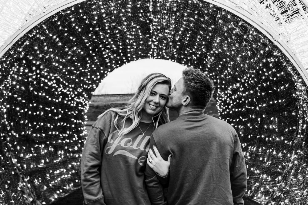 Couple embracing under an arch of twinkling fairy lights at night.