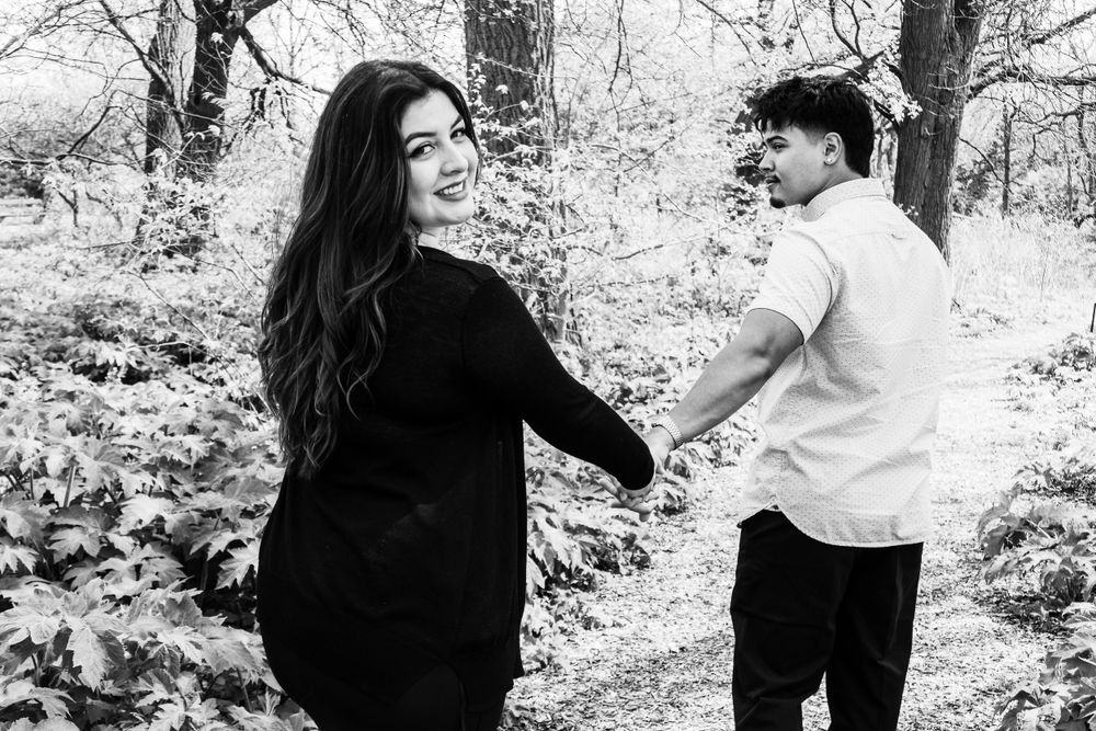A black and white photo of a couple holding hands in a wooded setting.