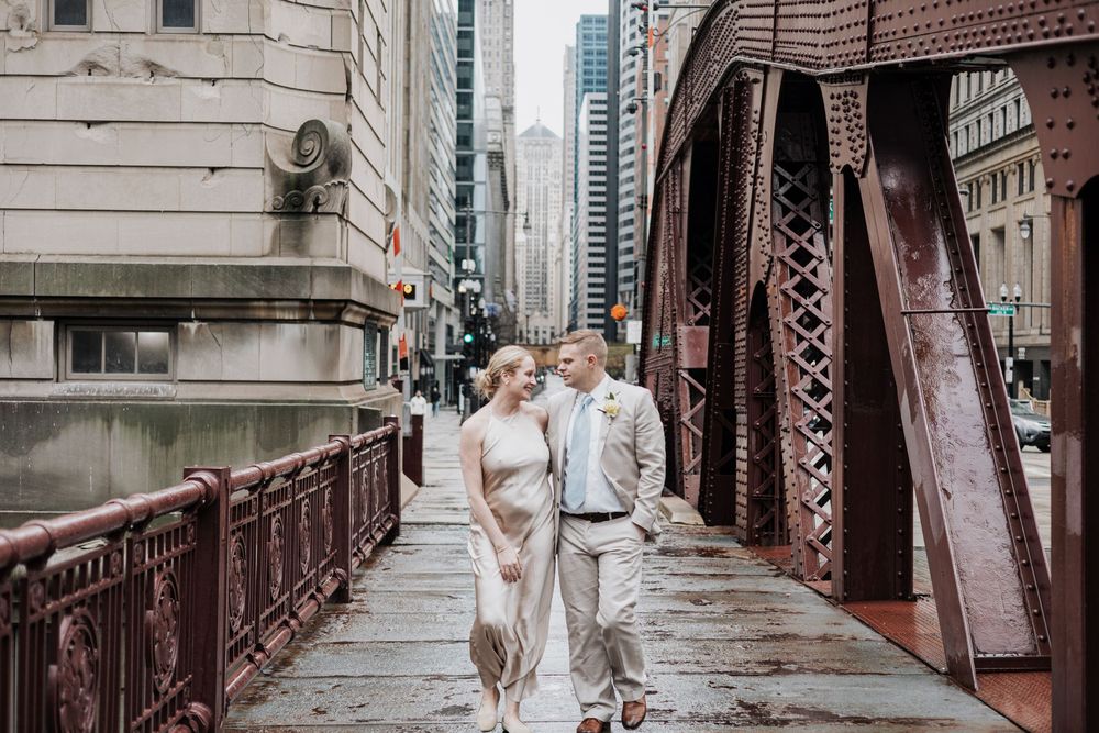 Couple walking on a historic Chicago bridge surrounded by city skyscrapers on a cloudy day.