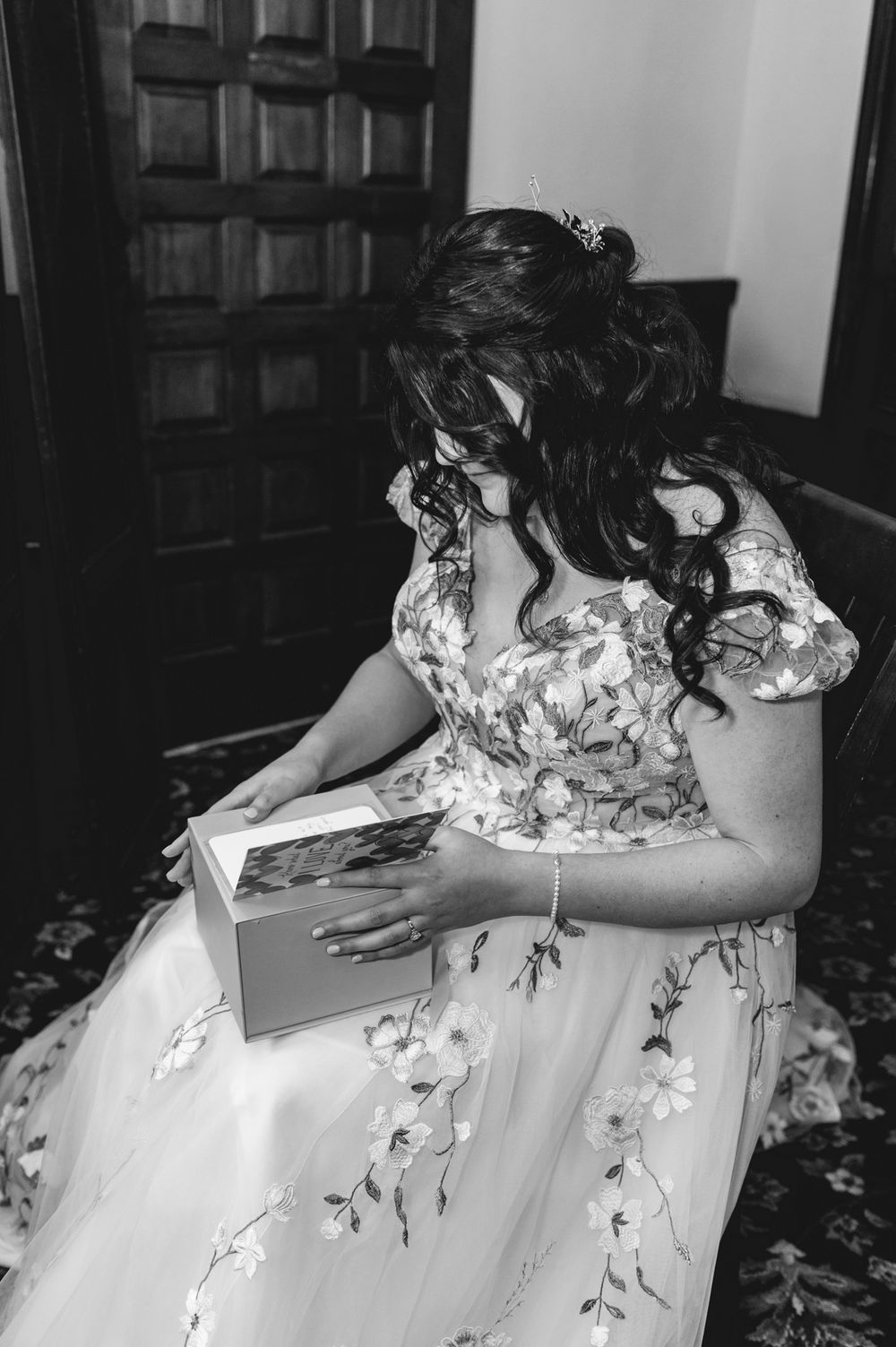 A person in a floral wedding dress looking at a book in black and white.