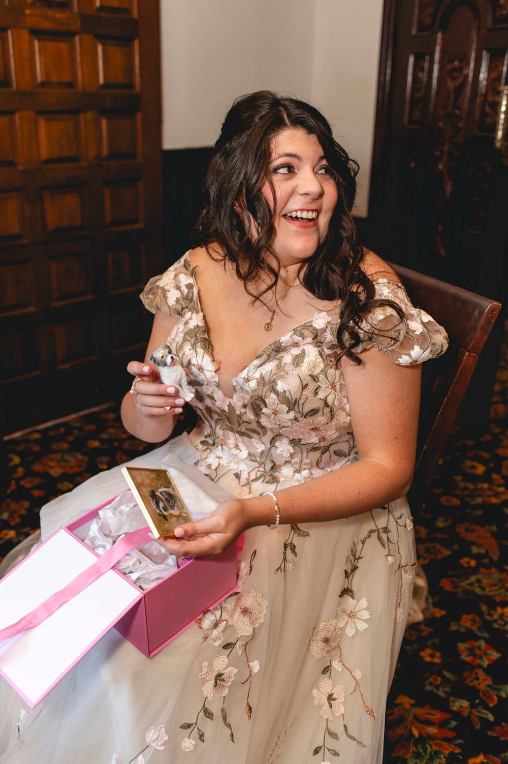 A person in a floral wedding gown joyfully opening a gift box.