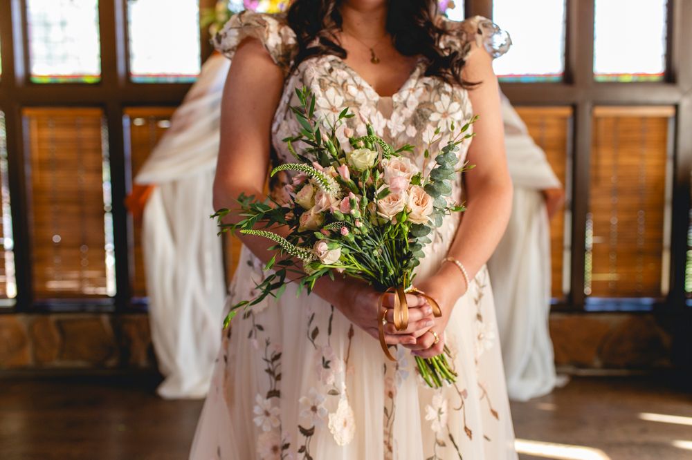 Close up of a delicate spring bouquet with pink flowers held against a lace wedding dress.