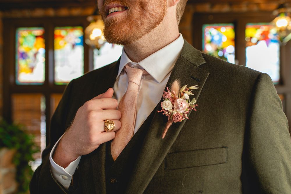 Close-up of a groom's olive suit with pink boutonniere and blush tie.