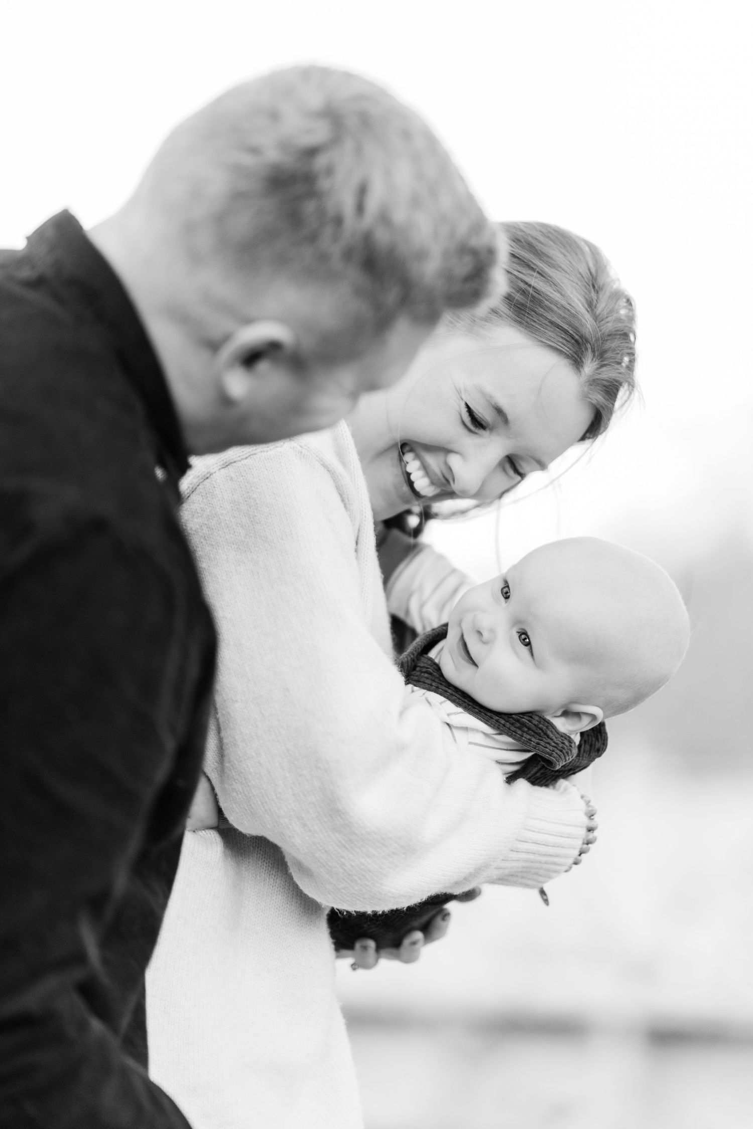 Black and white portrait of tender family moment with baby being held and embraced by parents.