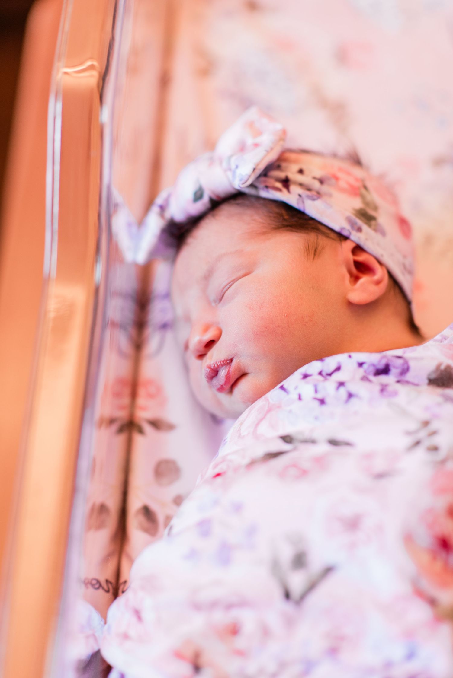 Sleeping newborn baby wearing floral headband in warm lighting.