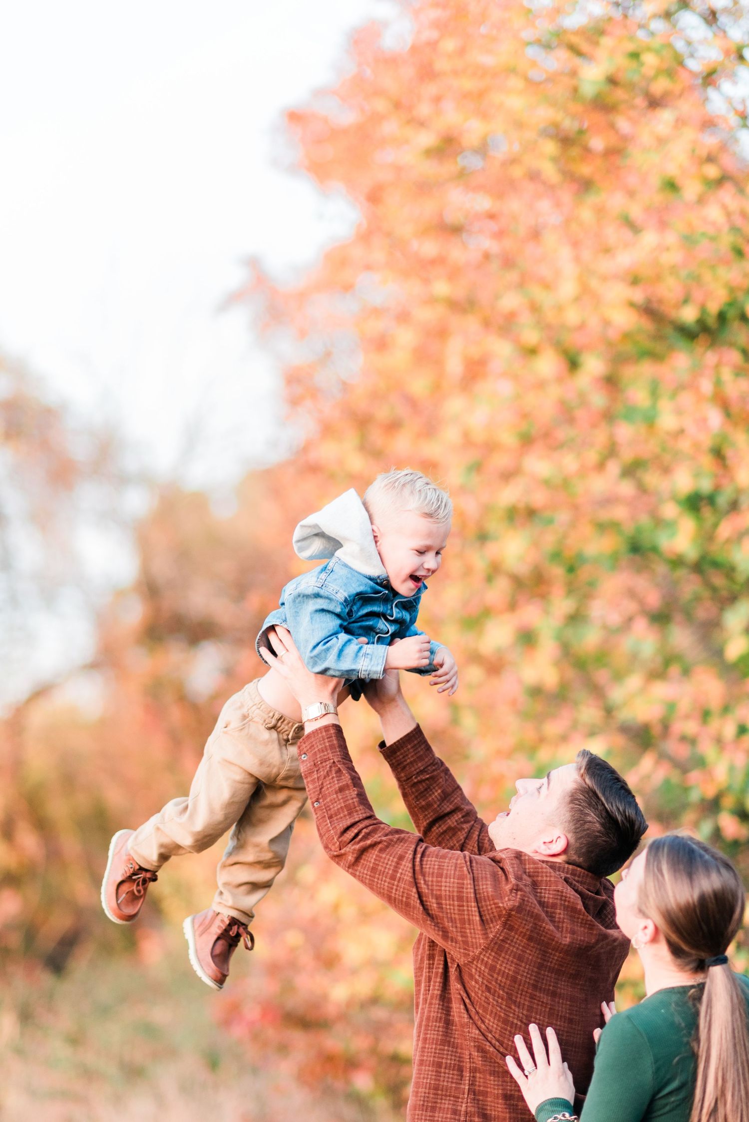 Family playing with baby outdoors during autumn with colorful fall foliage in background.