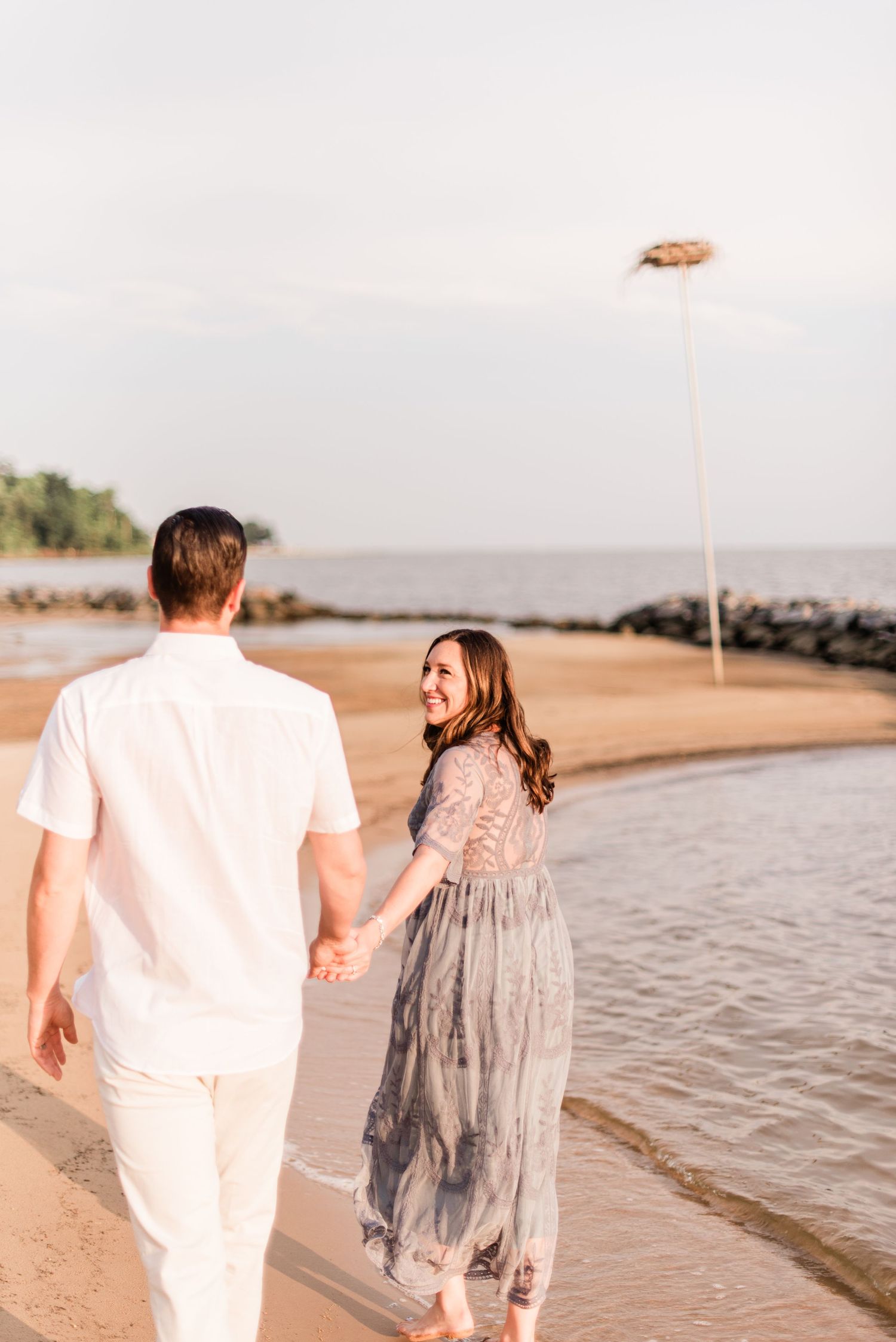Romantic couple walks hand in hand along beach shoreline at sunset.