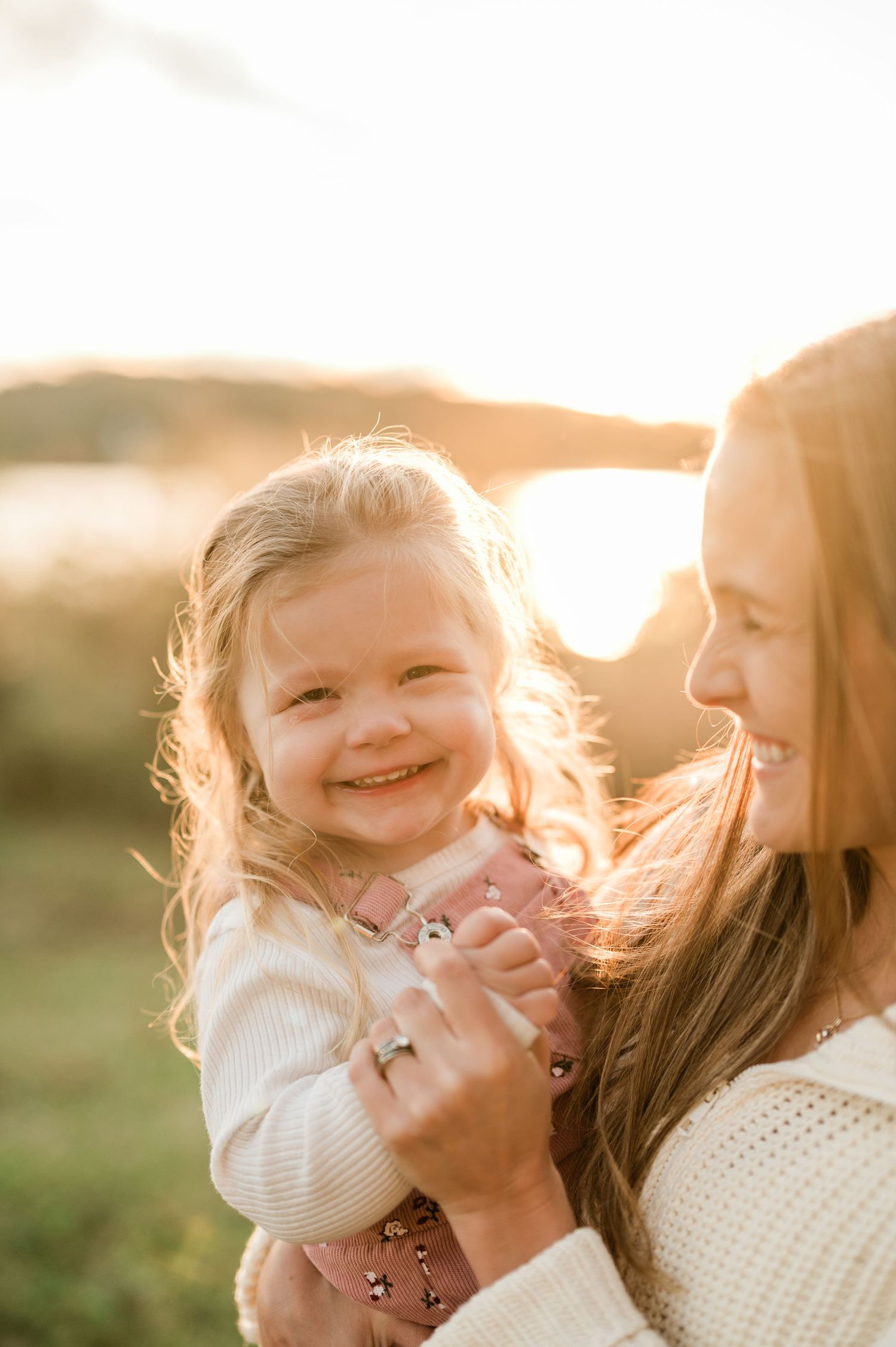 A heartwarming moment between parent and child laughing together in golden sunlight during an outdoor photo session.
