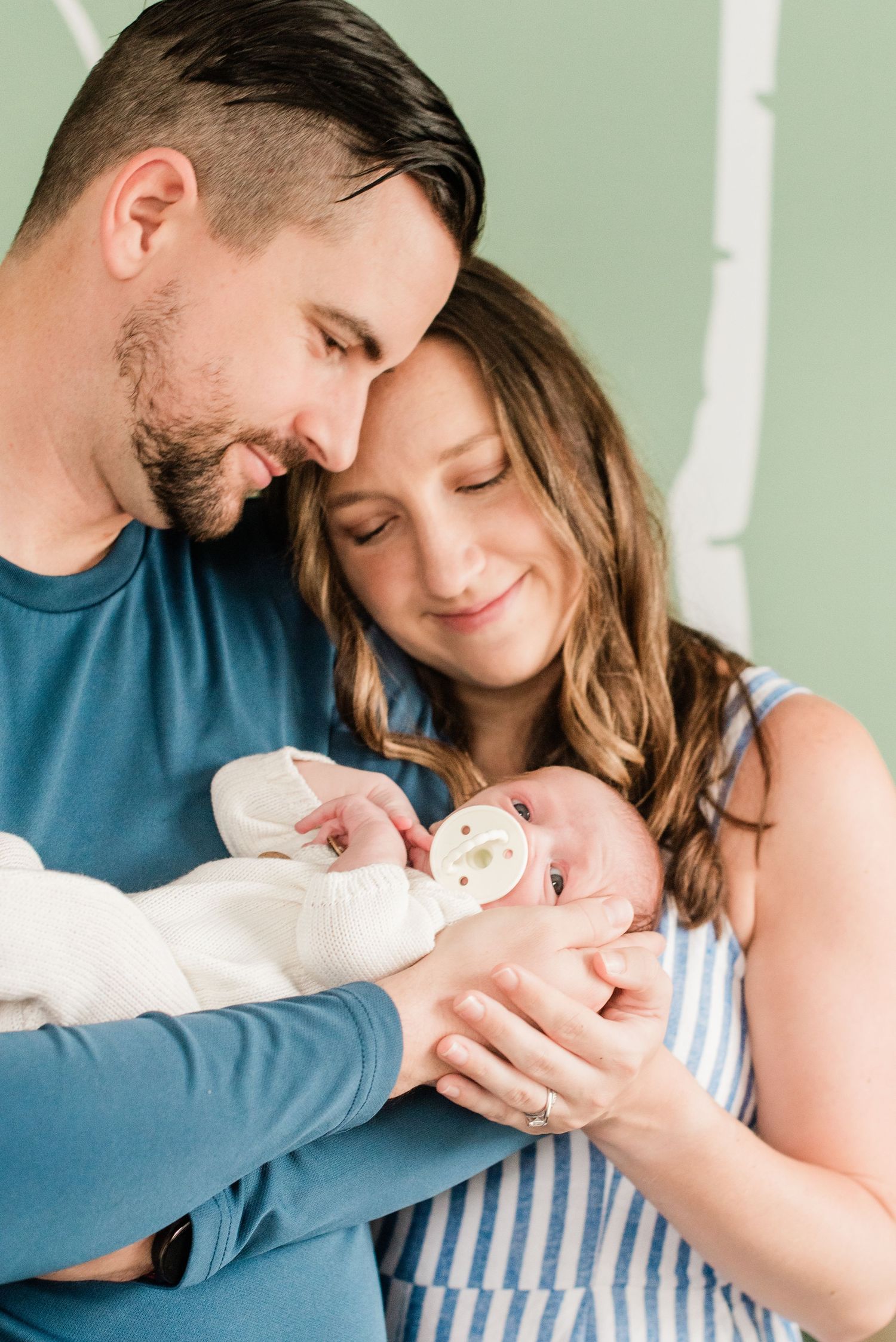 Intimate family moment as new parents cradle their newborn baby in a soft-lit indoor setting.