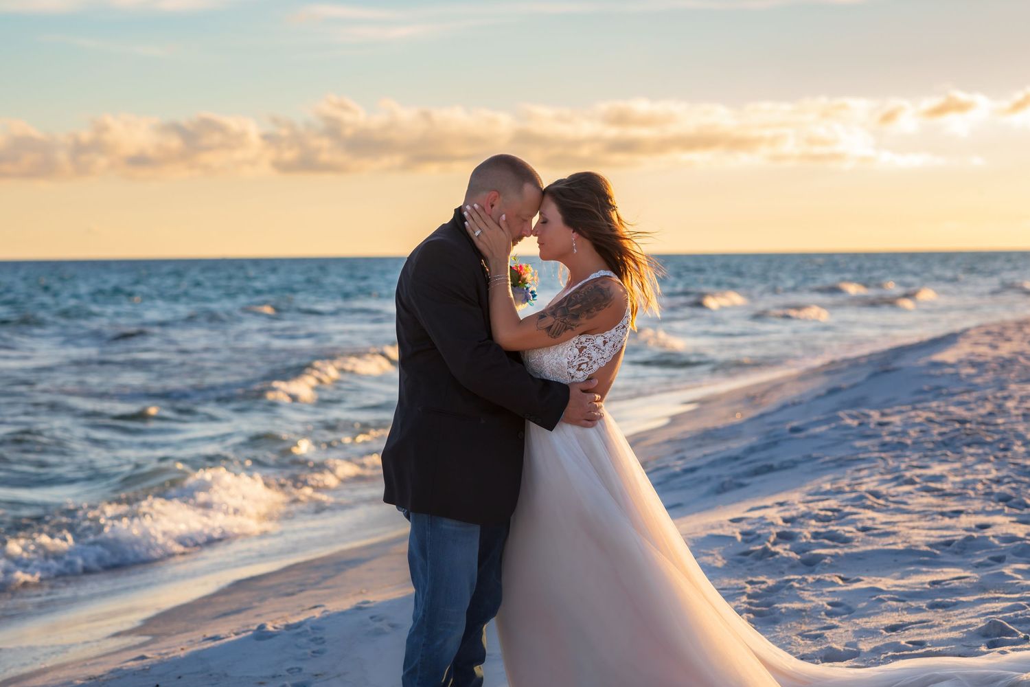 A couple shares a romantic kiss at sunset on a beach shoreline.