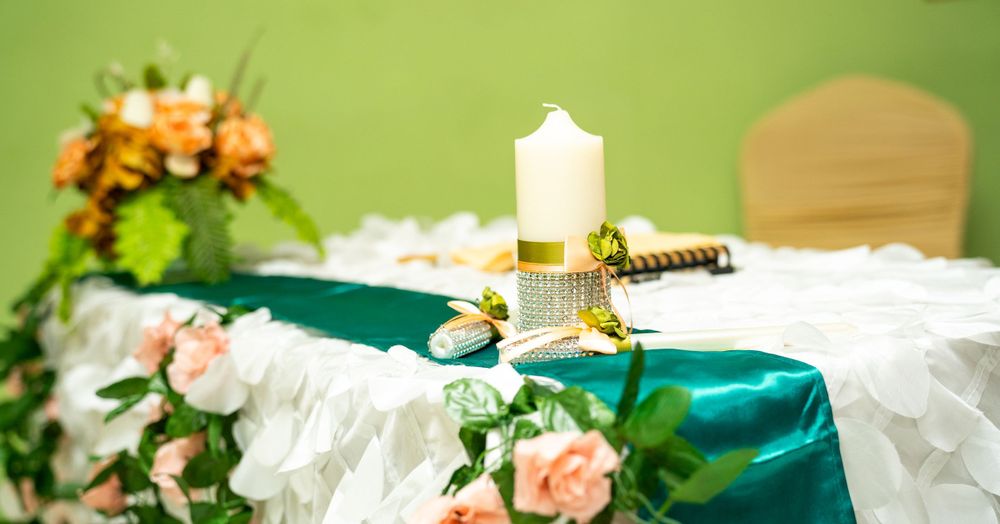 Decorative wedding table setting with candle, teal tablecloth and pink floral arrangements.