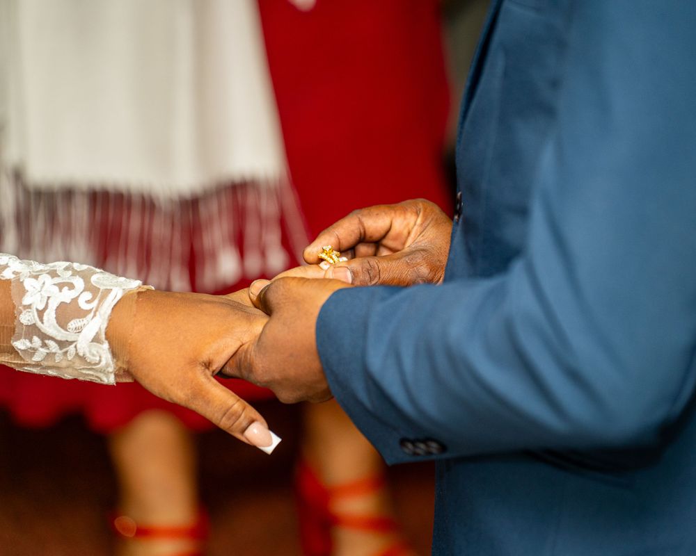Close-up of hands exchanging rings during wedding ceremony with white lace dress detail.