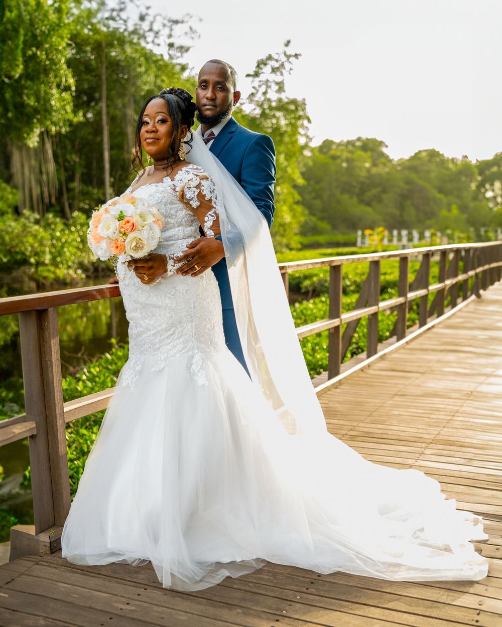 Wedding couple poses on wooden boardwalk surrounded by greenery.