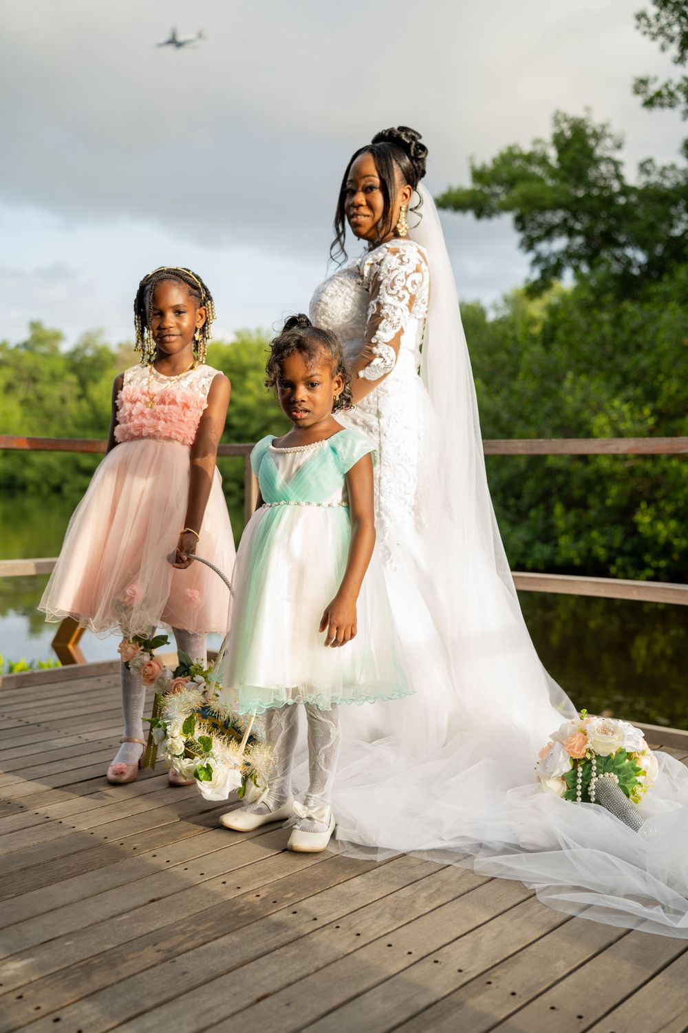 Three attendants in pastel dresses pose on wooden boardwalk during wedding.