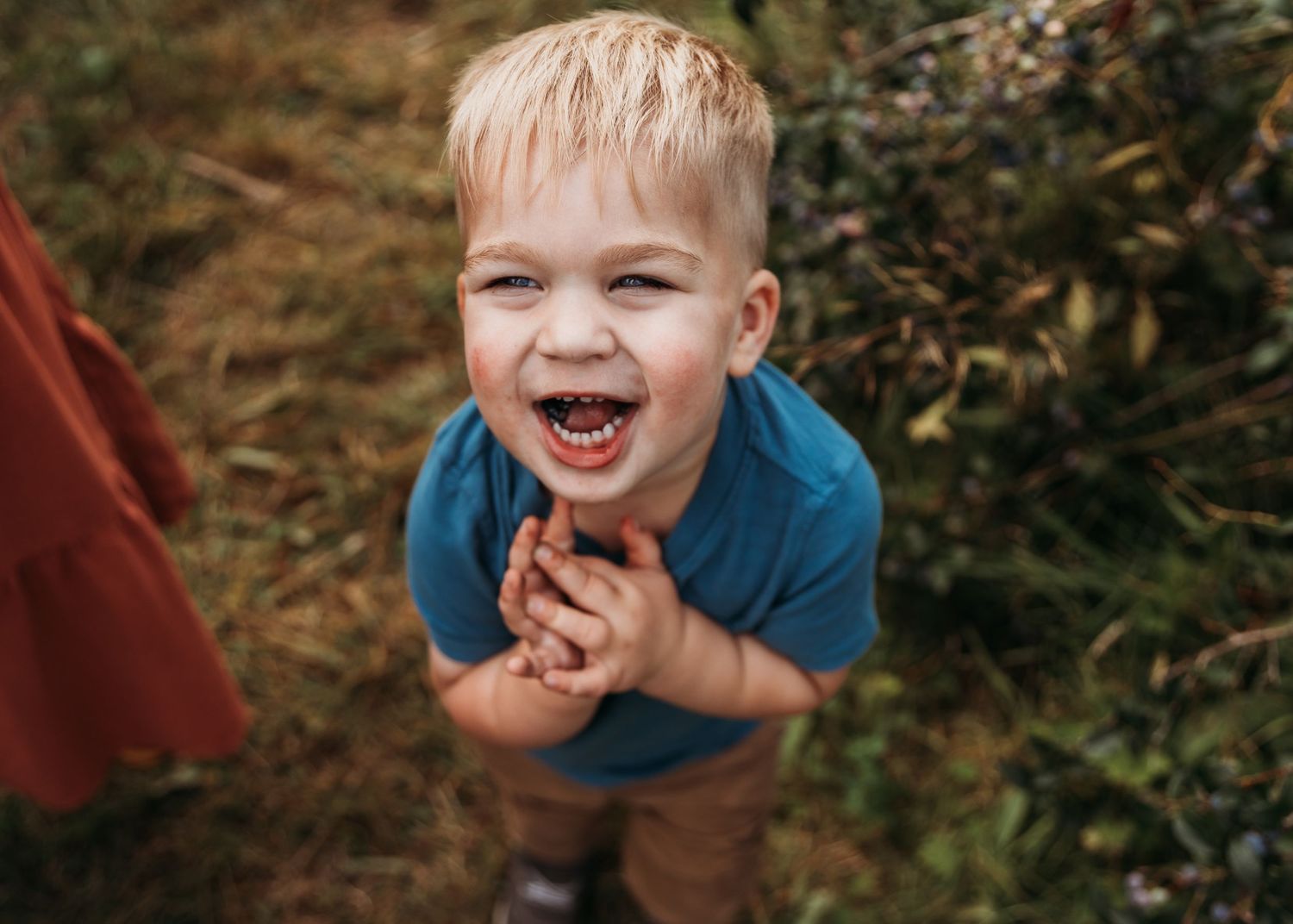 Young child in blue shirt laughing with joy outdoors.