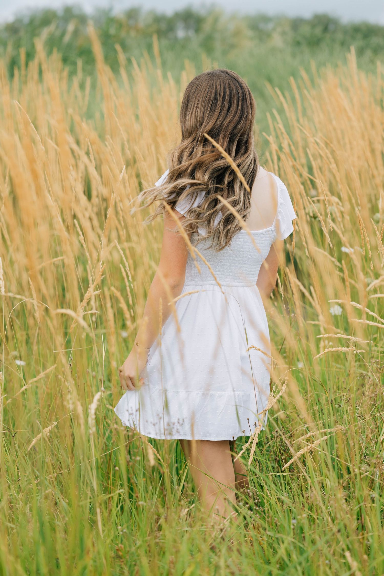 Young woman in a white dress walking through tall golden grass in a field.