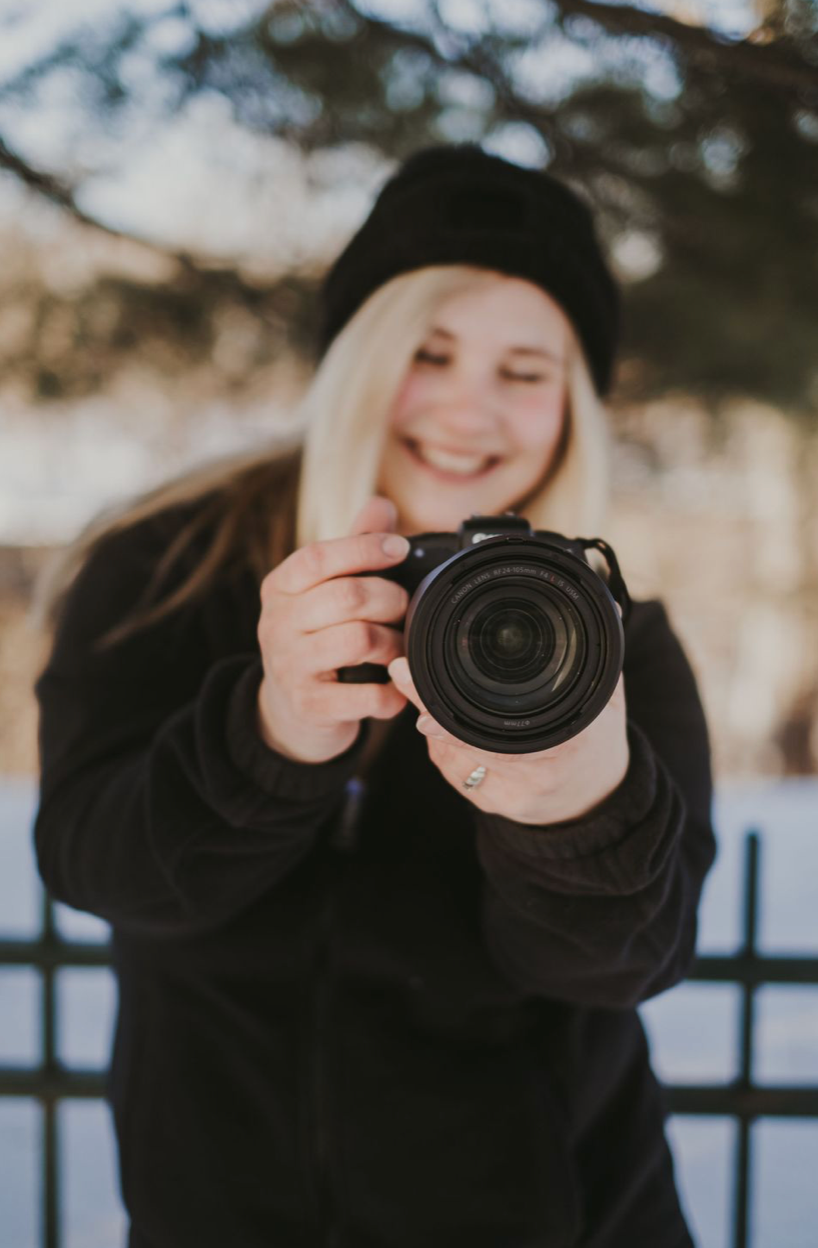 Person in black beanie holds camera while photographing outdoors.