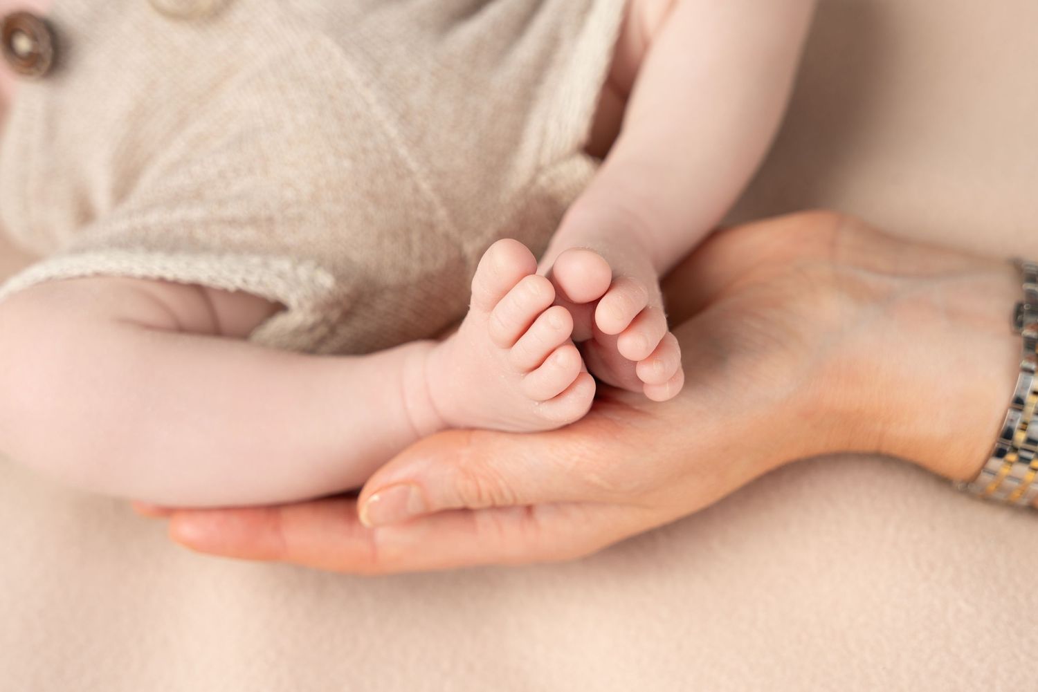 Close-up view of tiny baby feet resting in gentle adult hands against a soft beige background.