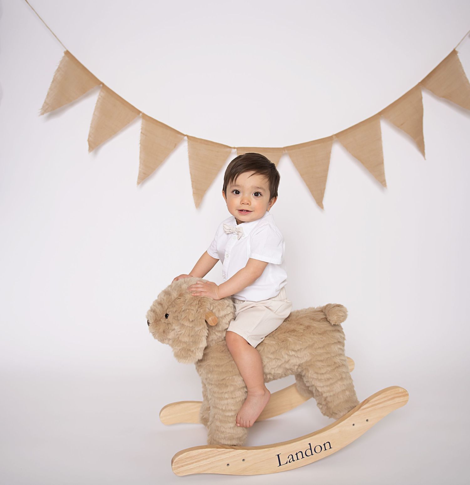 Baby sitting on personalized wooden rocking horse toy with triangle banner decoration in background.