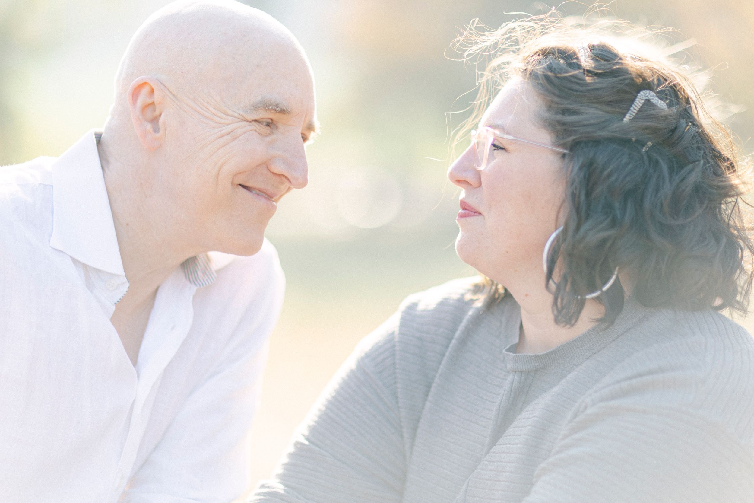 A couple shares a tender moment while laughing together in dreamy natural light.